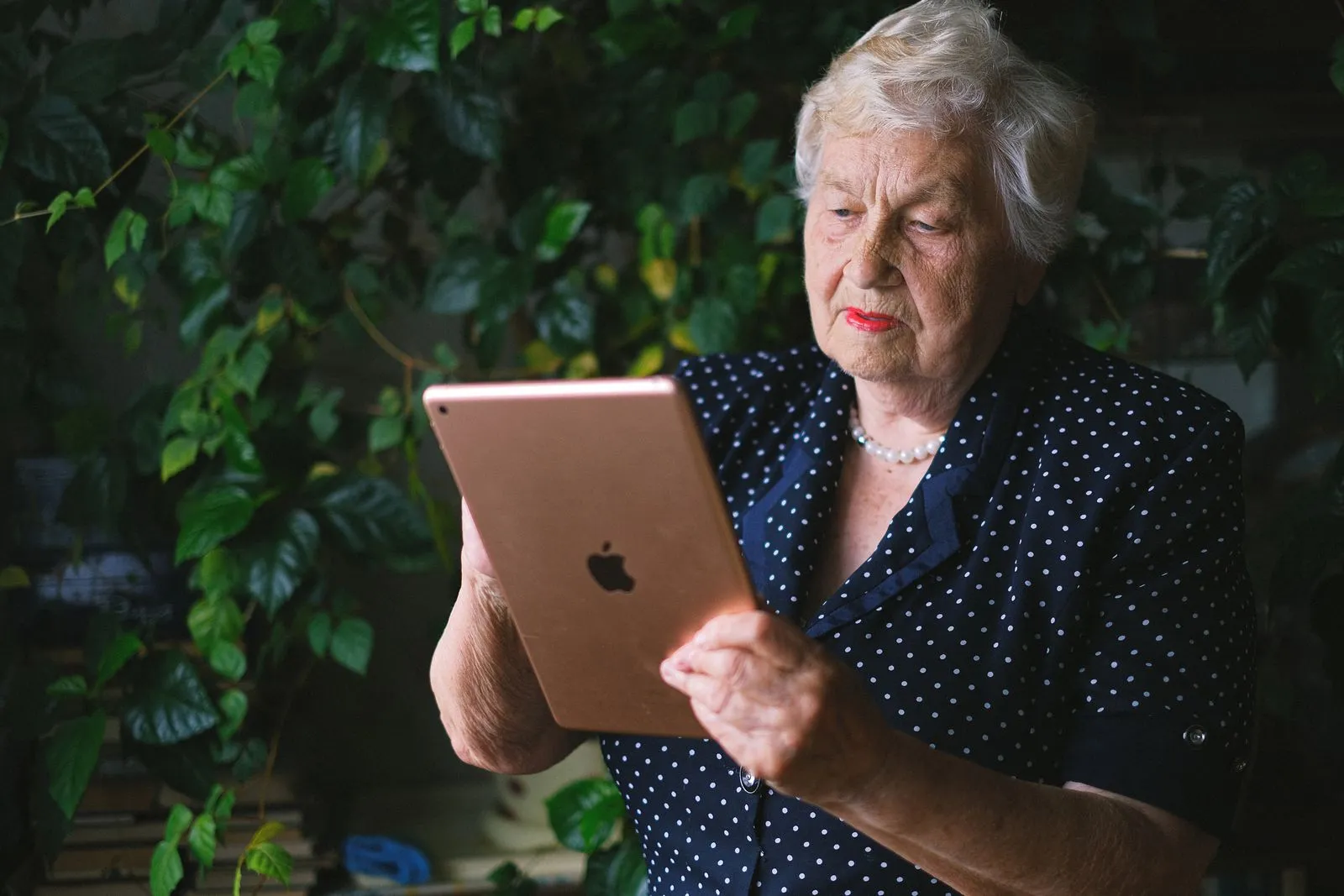 An elderly woman reading on a tablet in her garden