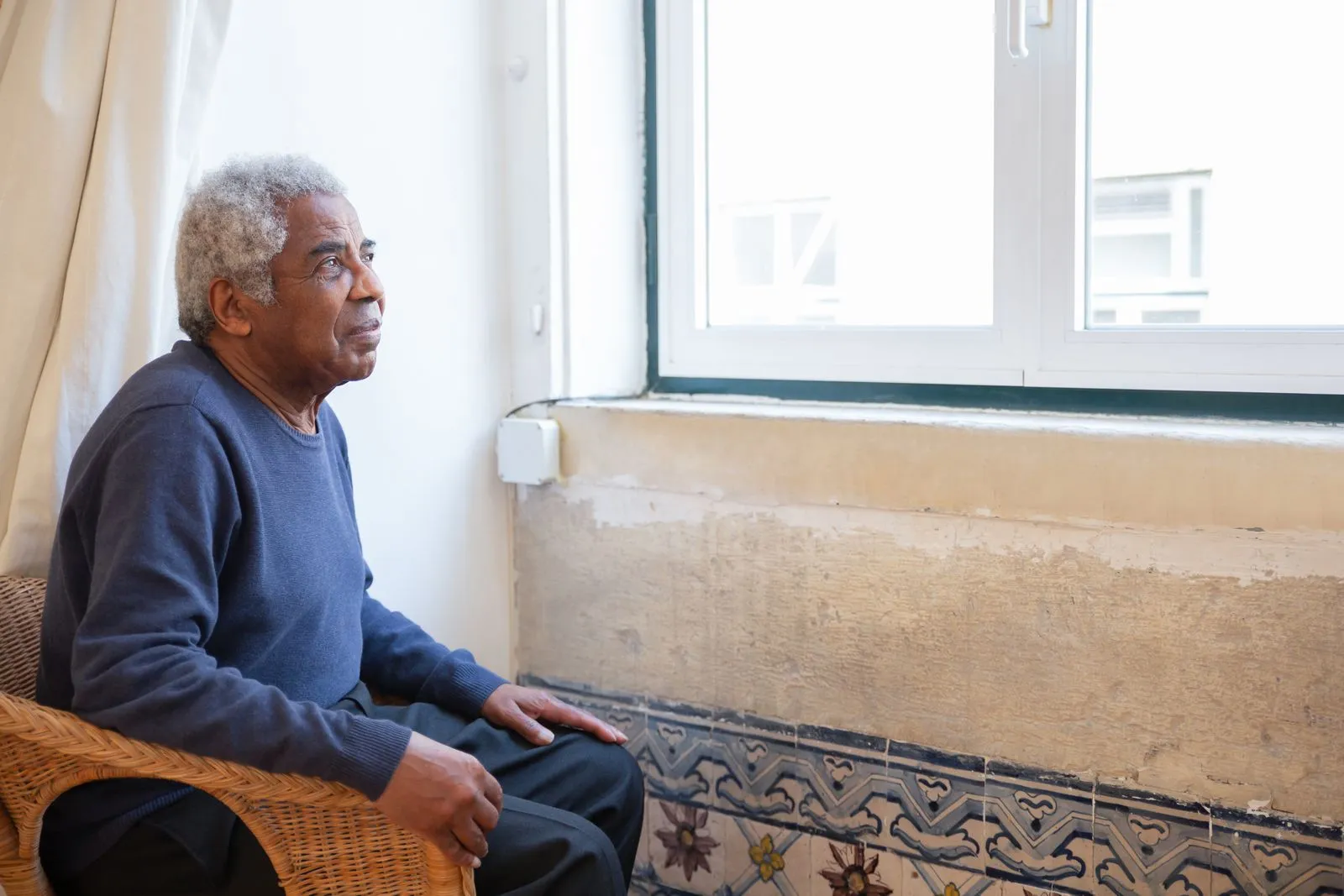 An elderly man sitting thoughtfully by his window